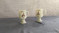 Pair of two white pedestal base mugs with gold print of Cinderella's Castle and personalization 'BOB' and 'JEAN'