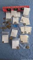 Wide view showing multiple coins and several labeled plastic bags containing coins sorted by country.