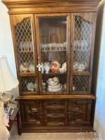 Front view of wooden china cabinet showing glass doors with lattice design, shelves inside with dishware, and lower storage drawers and cupboards