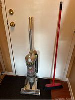 Full view of Hoover Air Sprint vacuum and adjacent red broom against a white door.