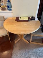 Drop-leaf kitchen table with light wood finish, pedestal base, set up without leaves extended