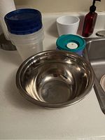 Wide view of the stainless steel mixing bowl, plastic Ziplock containers with blue lids, and Tupperware container with teal lid.