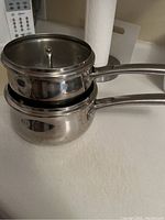 Two stacked stainless steel Kenmore pots with lids, showing shiny reflective metal surfaces and long handles.