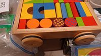 Close-up of a wooden wagon filled with colorful chunky wooden blocks. Wagon has four wooden wheels and a pull rope.
