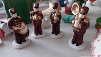 Four-piece miniature band Christmas ornaments with musicians holding drum, accordion, trumpet, and clarinet in maroon uniforms and white bases