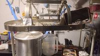 Metal hanging kitchen pot rack with two lights on top, hooks along sides, holding various kitchen items including a large tamale pot with lid and clear plastic pitcher underneath.