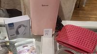 Front view of Astro AI mini fridge in pink, neck massager box, makeup mirror, and foot care items.