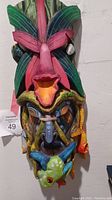 Front view of the tall colorful carved balsa wood mask with animal and leaf motifs.
