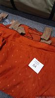 Photo showing the orange sound-proofing drapery laid out flat with visible snap closures and fabric straps.