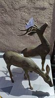 Pair of brass deer figurines, doe in front with lowered head and buck behind with raised head and antlers