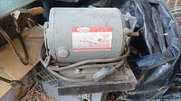 Dayton motor mounted on black base, with electrical cord coiled around it, showing some wear and dirt.