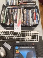 Photo showing a black container filled with 40+ assorted DVD movies including titles by Pixar and Disney, ASUS keyboard and grey wireless mouse, Clear TV HDTV indoor antenna packaging visible at the bottom