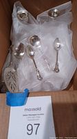 Photo showing two sterling weighted candlestick holders by Duchin and assorted antique sterling silverware including spoons and pie server, wrapped in protective cloth inside a box.
