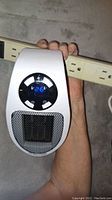 Close-up photo of one white plug-in wall outlet heater showing digital LED display with temperature set to 26 degrees.