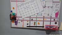 Whiteboard image showing calendar layout, two magnetic baskets holding markers, assorted magnets attached to board.