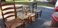 Four antique wooden chairs with rush seats arranged outdoors showing different wood finishes and seat styles.