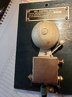 Close-up side view of vintage electric bell with manufacturer's plate, mounted on dark surface.