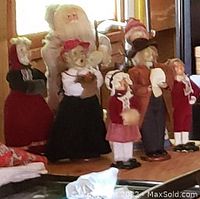 Seven Byers Choice Caroler and Santa Claus figures displayed on a wooden surface in front of a window, showing front and side views of the figurines.