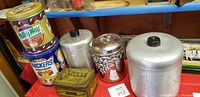 Photo showing stacked Milky Way and Snickers branded tins with rectangular Best Cut Plug tin and three aluminum canisters on red surface.