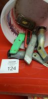 Image showing carpet cutting utility handles in a bucket with blades, some metal and some plastic, placed on a red surface with item tag 124