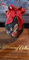 Close-up of a dark Christmas ornament painted with Santa and a red ribbon bow on top, showing detailed artwork.