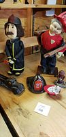 Photo showing two fireman figurines, antique metal fire truck, fireman helmet bank, dog figurine with hydrant and fire hydrant decoration on wood table.