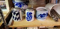 Photo showing three German salt glaze stoneware pottery pieces: two lidded steins with pewter lids and one open jar, each with cobalt blue decoration.