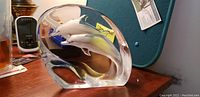 Front view of clear crystal glass paperweight showing two white dolphins jumping inside, sitting on a wooden surface.
