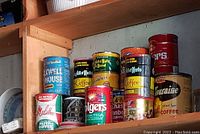 Photo showing multiple vintage coffee tins on a shelf, including Folgers, Melitta, Shaw's, and others.