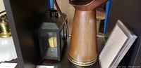 Photo showing a black metal lantern with glass and candle inside, tall copper pitcher with brass accents, and a silver picture frame.
