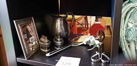 Silver plated items including two table top lighters, pitcher, cake cutter, sugar and creamer set, and picture frame arranged on a shelf.