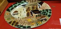 Decorative ceramic turkey platter with painted farm and harvest scene placed on a red surface.