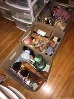 Overview of three cartons filled with various household items, including wood art, lamps, and books on a wooden floor.