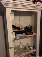 Full view of the white wooden bookshelf with items on shelves, showing wear and tear on paint, glass bowls, ceramic figurines, and metal decorative items.