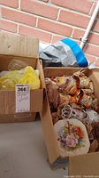 Two cardboard boxes containing assorted china and glassware with decorative floral and geometric patterns