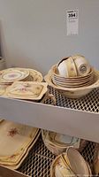 Top shelf with stacked bowls, cups, and plates, showing floral design and gold accents.