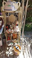 Three shelves holding assorted decor items including ceramics, figurines, wooden box, plates, and small decorative objects under natural light.