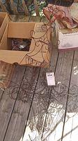 Photo of three brown wire garden art pieces laid on wooden deck near cardboard boxes showing scroll work design