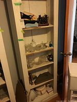 White cabinet with multiple shelves holding glass decor items, figurines, and other objects.