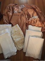 Photo showing eight white pillow shams with floral patterns and two copper satin-like Nicole Miller branded covers.
