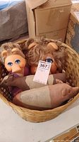 Two Miss Piggy dolls with curly hair inside a straw basket, also containing fabric pig and cow plush toys.