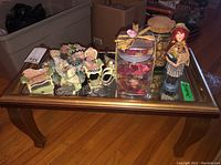 Shelf with mirror surface displaying ornaments including ceramic birds, teapots, dried potpourri jars, and a ceramic doll on a wooden floor.