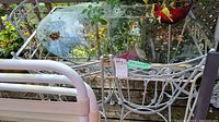 Photo showing oval glass top metal table and portion of the four white metal chairs around it, with visible wear and rust on metal parts.