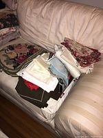Various folded table linens including napkins and cloths in multiple colors and patterns on a beige couch.