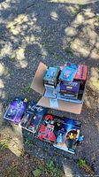 Lot of boxed and loose figures and bobbleheads outdoors on a pavement surface with shadows from nearby trees.