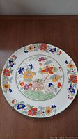 Full view of the large circular plate showing the colorful hand-painted floral design and central Bible pattern scene.