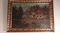 Full view of the oil on canvas painting in an ornate golden frame. Depicts a rustic cabin with trees and a mountainous background.