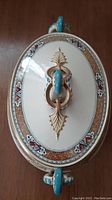 Top view of antique Till & Sons lidded serving dish showing ornate handle and decorative border decals with gold, turquoise, and red details on cream ceramic base.
