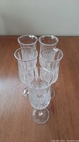 Top view showing five clear cut crystal champagne flutes arranged in a group on a wooden surface.