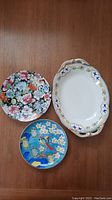 Overview of three hand-painted ceramic plates showing different floral and bird designs
